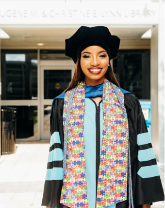 Dr. Lewis-Hunte smiling and posing in her full graduation garb outside of a university building